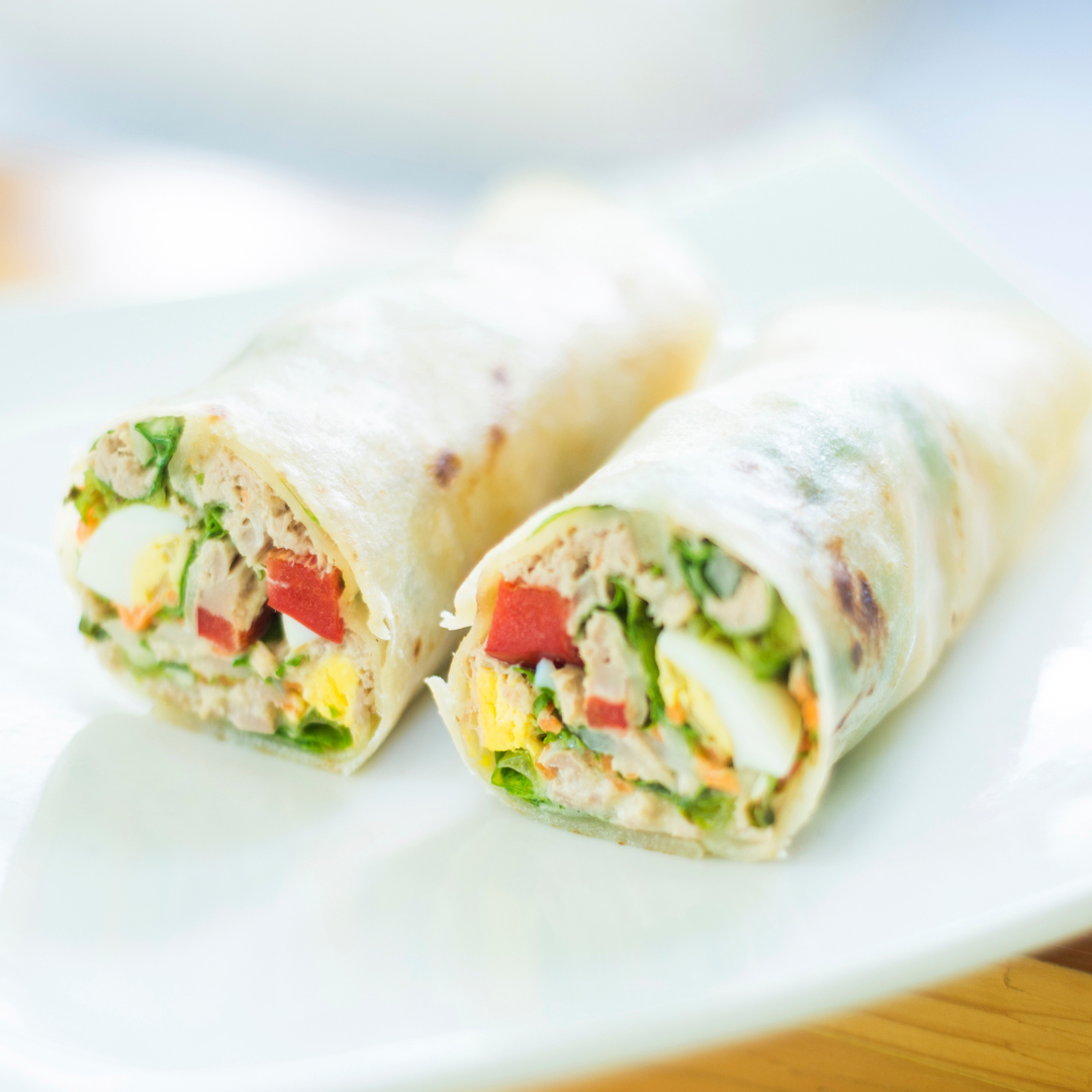 Two tortilla rolls filled with eggs and vegetables. The rolls are cut in half and served on a white plate.