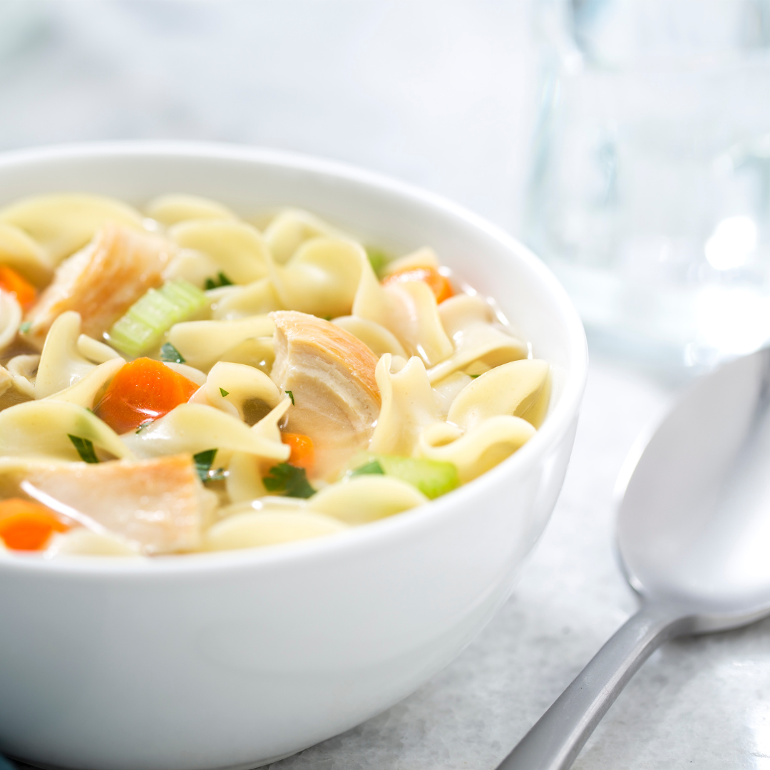 A bowl of chicken noodle soup with tender chicken, egg noodles, carrots, and celery in a clear broth.