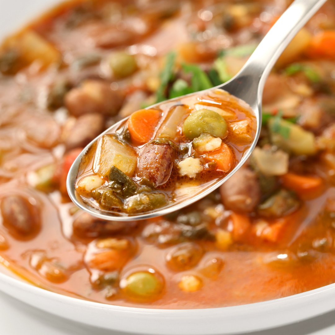 A spoon full of minestrone soup, showing various vegetables like carrots, peas, beans, and noodles in a rich broth.