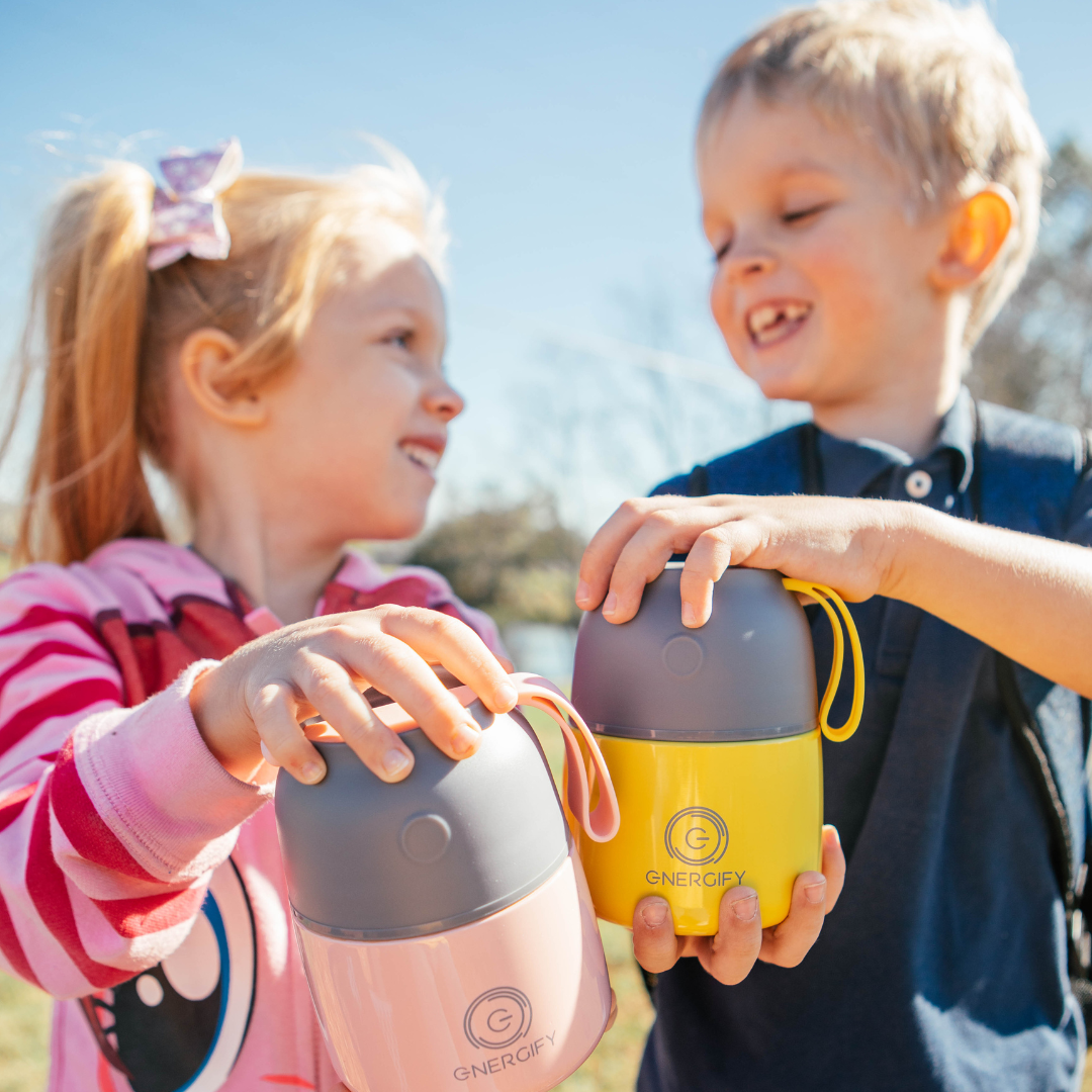 Young boy and girl about 6-8 years old holding 12 oz Antique pink and Starfruit Yellow Energify food jars, they are smiling to each other.