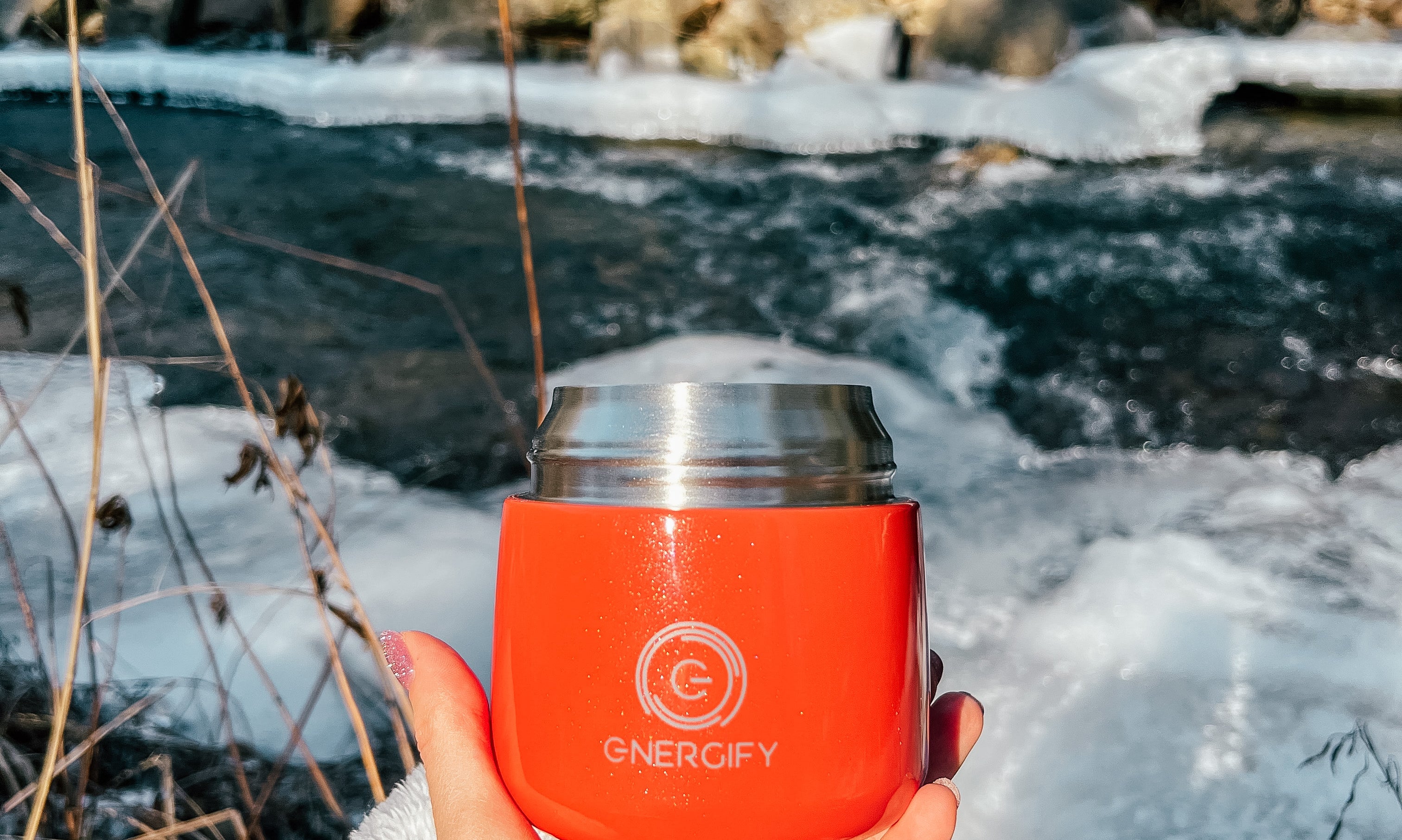 A woman's hand holding 12 oz Fusion Coral Energify vacuum insulated food jar. In the background there is a frozen river and snow.