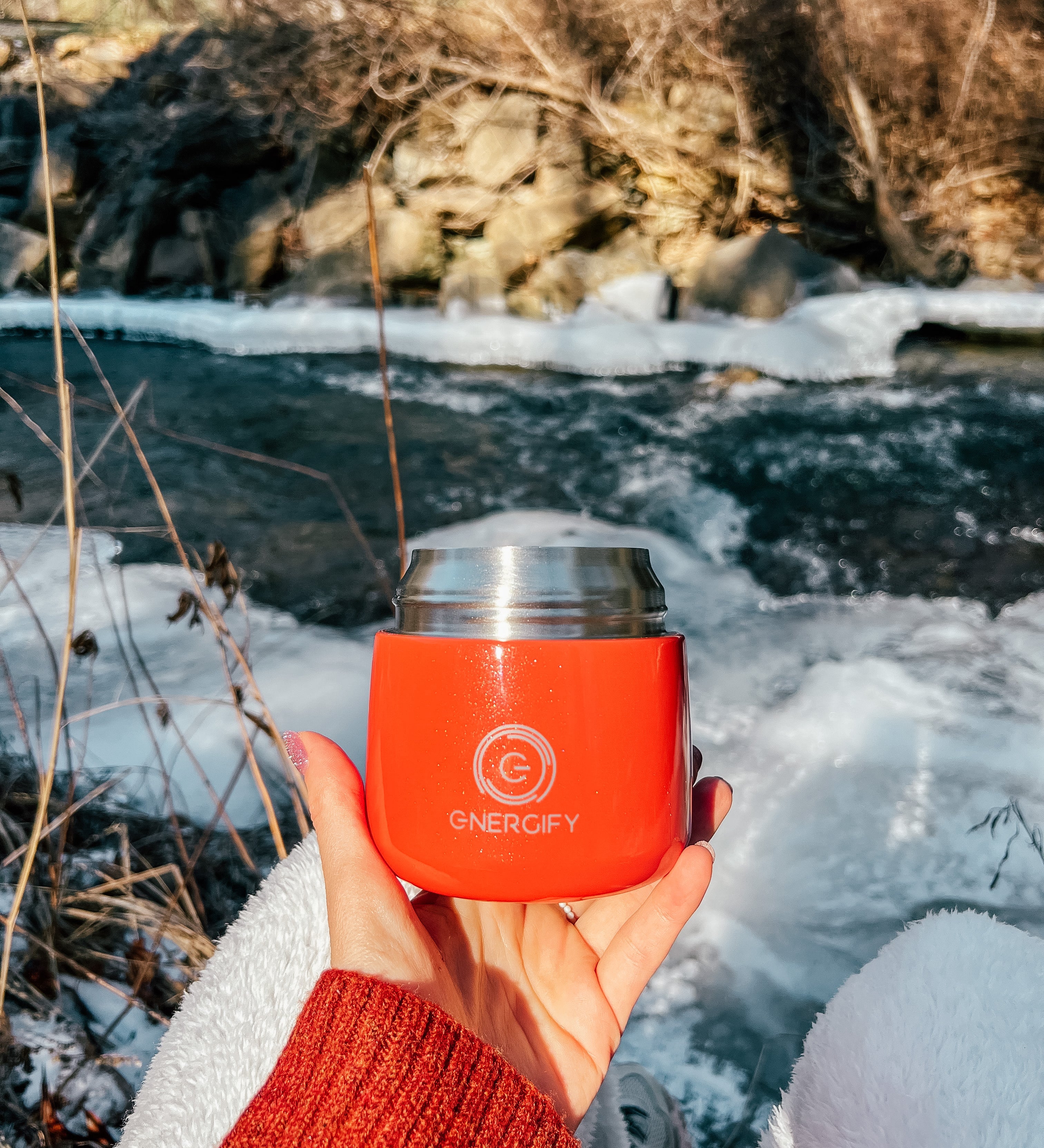 A woman's hand holding 12 oz Fusion Coral Energify vacuum insulated food jar. In the background there is a frozen river and snow.