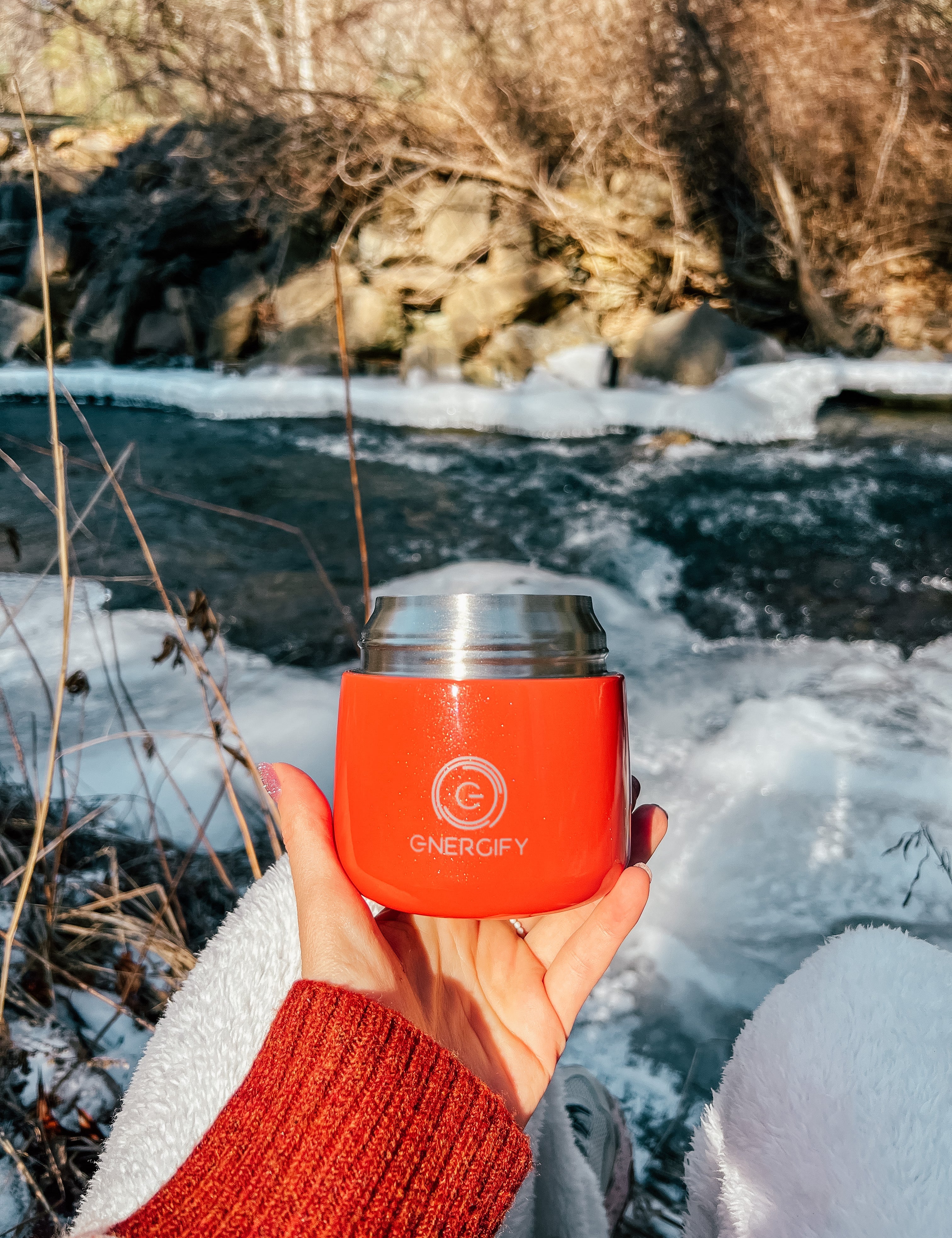 A woman's hand holding 12 oz Fusion Coral Energify vacuum insulated food jar. In the background there is a frozen river and snow.