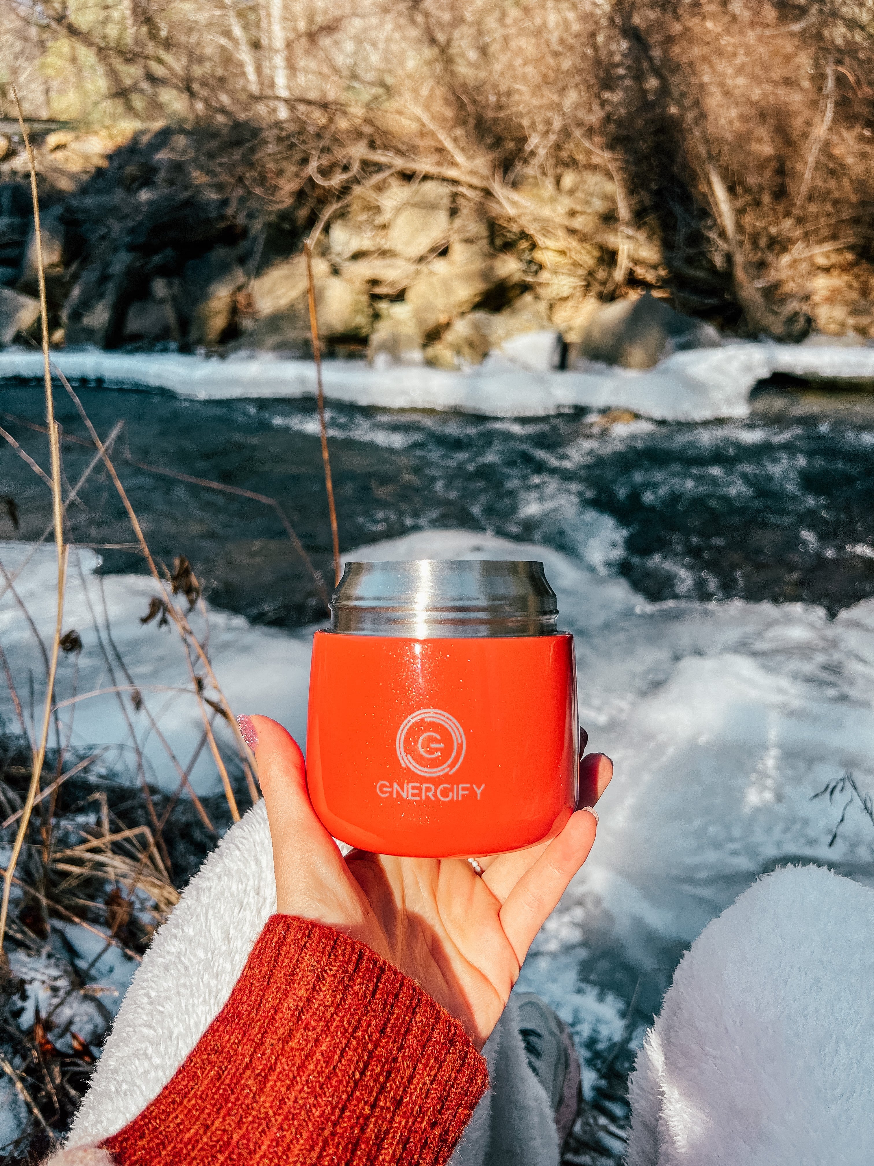 A woman's hand holding 12 oz Fusion Coral Energify vacuum insulated food jar. In the background there is a frozen river and snow.