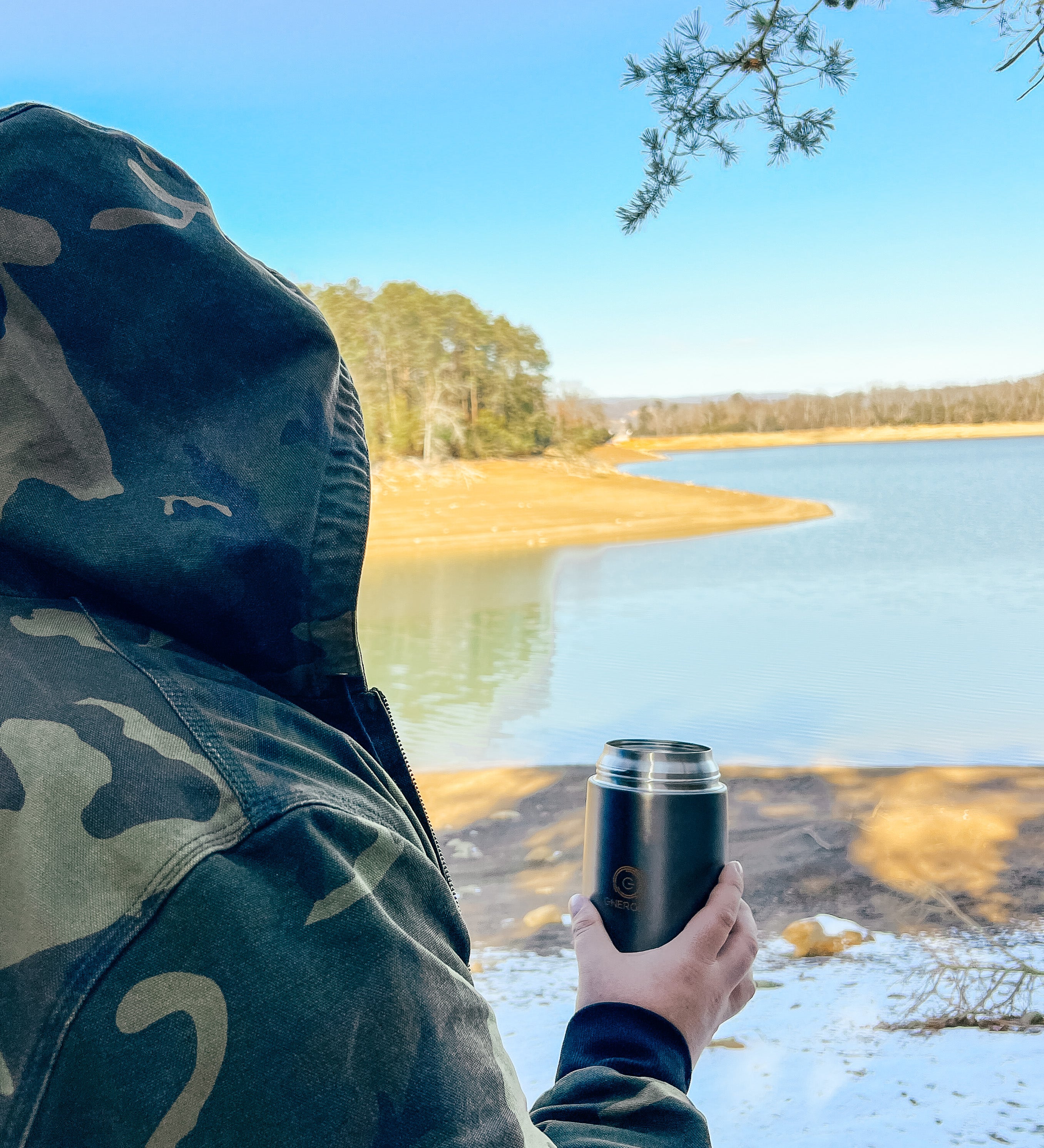 A man in a camo jacket and hood  on his head is holding in his right hand 24 oz Energify vacuum insulated food jar in Gray color. 