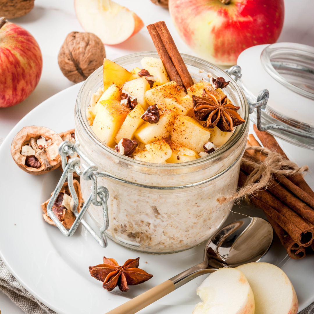 A glass jar filled with oatmeal topped with chopped apples, walnuts, cinnamon sticks, and star anise. The oatmeal is creamy and appears to be cooked overnight.